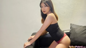 Pretty Asian babe poses on couch in panties and shirt